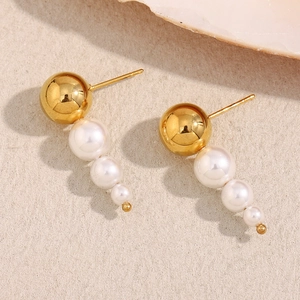 Close-up of 18K gold plated pearl earrings with three cascading white pearls on beige