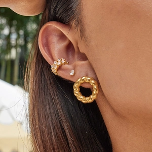 Close-up of gold rope hoop earrings and gemstone studs set on a female model