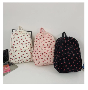 Three corduroy strawberry backpacks in white, pink, and black colors on a white desk