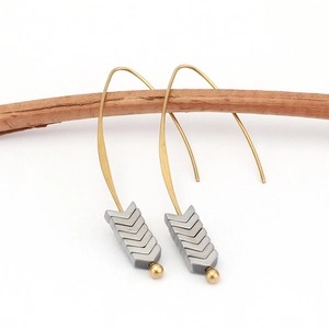 Minimalist gold ear hooks with grey arrow pendants displayed on a natural wooden branch