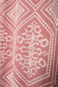 Close-up of geometric white embroidery on pink cotton linen fabric with ethnic patterns