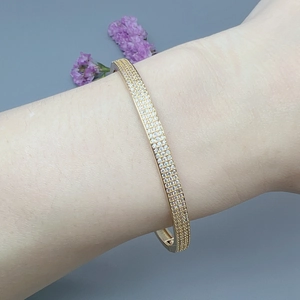 Elegant gold-plated bangle bracelet with micro-paved cubic zirconia on blue background