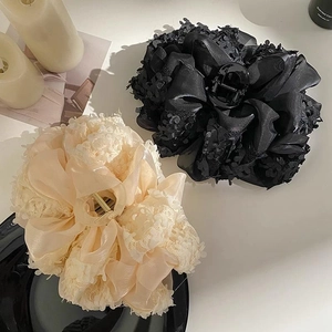 Détail de grandes pinces à cheveux à fleurs en dentelle noire et champagne sur fond blanc