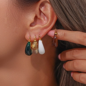 Close-up of model wearing gold earrings with green, amber, and white resin drops