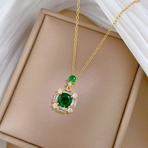 Close-up of golden necklace with emerald-green center stone in beige jewelry box