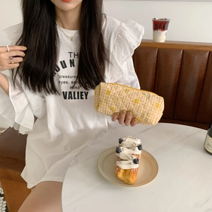 Detailed lifestyle view of a yellow checkered quilted cosmetic pouch held by a person
