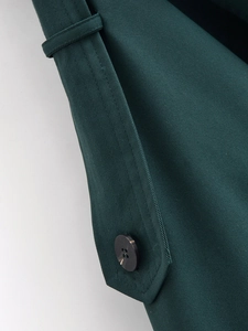 Detailed close-up of dark green trench coat cuff featuring twill fabric and button detail