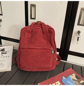 Detailansicht eines roten Cord-Rucksacks mit Reißverschlusstasche und Tragegriffen