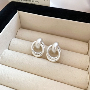 Close-up of matte silver geometric multi-layer hoop earrings in a beige jewelry box