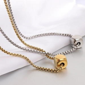 Macro shot of silver and gold polished cube pendant on a minimalist box chain necklace