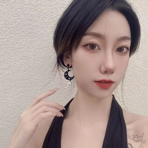 Detail of a black moon and star drop earring with a round white pearl on model