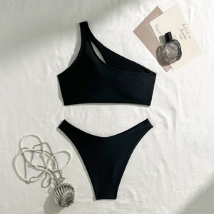 Flat lay of black one-shoulder cutout bikini with pearl shell necklace on textured background
