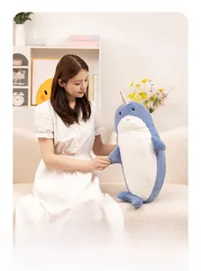 Detail of blue narwhal plush toy with silver spiral horn held in a cozy home setting