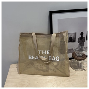 Detail of khaki mesh beach tote bag with 'THE BEACH BAG' text on a wooden table