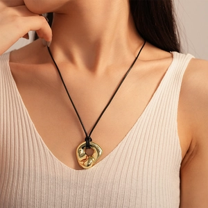 Detailed close-up of a polished gold irregular pendant on a black woven cord necklace