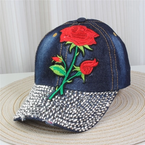 Detailed embroidery of a red rose and sparkling rhinestones on a blue denim baseball cap