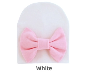 Close-up of white cotton newborn baby hat with large pink bow detail and soft knit texture