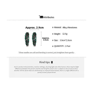 Detailed view of C-shaped earrings with dark green rhinestones and silver needles