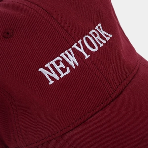 Dettaglio ravvicinato del ricamo bianco NEW YORK su un cappellino in cotone bordeaux