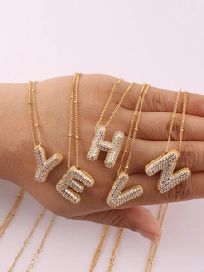 Macro detail of gold bubble initial necklaces with cubic zirconia on a beaded chain