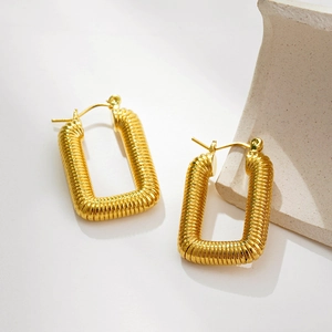 Detailed close-up of gold rectangular earrings with textured spiral pattern and metallic glow
