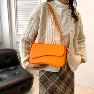 Minimalist bright orange leather crossbody bag with curved flap shown on model in studio