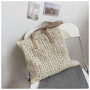 Detailed texture of handwoven hollow pattern on off-white straw tote with brown leather strap