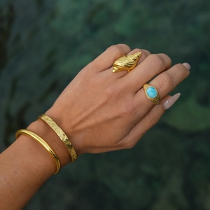 Close-up of golden ocean-textured seashell rings and bracelets with Larimar stone