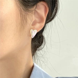 Close-up of iridescent heart stud earring with pearl luster on a model's ear