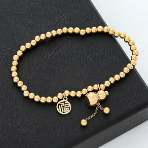 Detail of gold bead bracelet with Fu character pendant and gourd charm on black leather