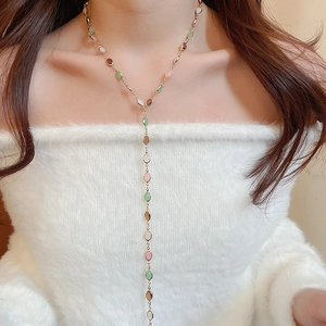 Detail of Y-shaped gold necklace with colorful oval beads on a model wearing white
