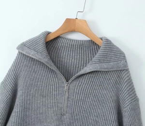Close-up of grey knit sweater with half-zip collar and ribbed texture on wooden hanger