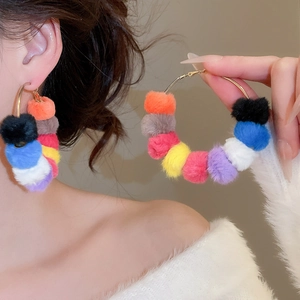 Close-up detail of large gold hoop earrings featuring multi-colored fluffy plush pom poms