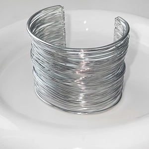 Exaggerated silver multilayer wire open bangle on a white ceramic plate top view