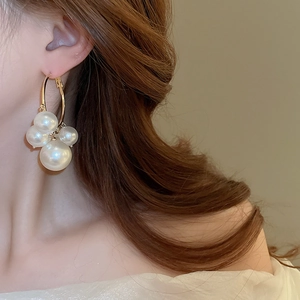 Detail view of large gold hoop earring featuring elegant clustered white pearls on a model