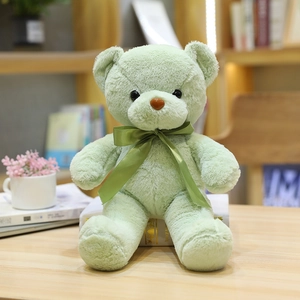 Lindo oso de peluche verde claro con lazo verde sentado sobre un escritorio de madera