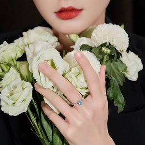 Elegant silver open ring with oval blue topaz gemstone on model's hand with flowers