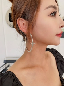Detail of silver hoop earring featuring a zircon-encrusted cross pendant on a model
