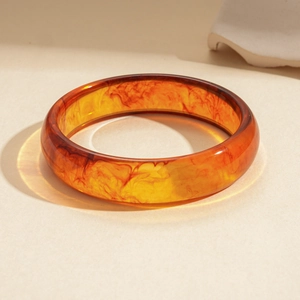 Close-up of translucent amber resin bangle featuring artistic dark red swirl textures