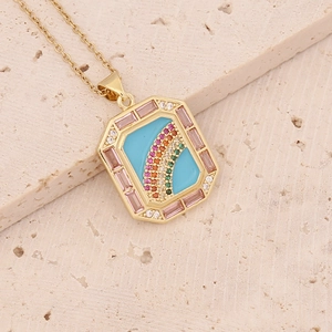 Macro shot of 18K gold pendant featuring blue enamel rainbow and pink gemstone border