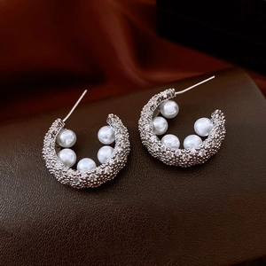 Macro shot of silver C-shaped earrings with micro-set zircons and elegant white pearls