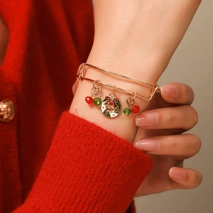 Close-up of adjustable gold Christmas bracelet with wreath charm on a red sweater background