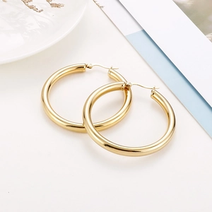 Detailed view of polished 18K gold hoop earrings on a decorative white ceramic tray