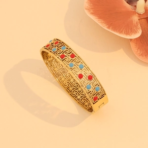 Vintage hollow gold bangle with red and blue enamel and geometric patterns on warm background