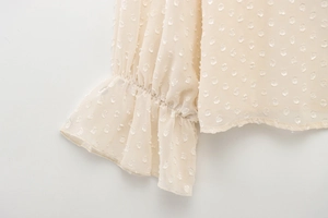 Detail of ruffled cuffs and pleated chiffon texture on a cream polka dot blouse
