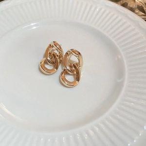Golden double chain drop earrings displayed on a white textured ceramic jewelry dish