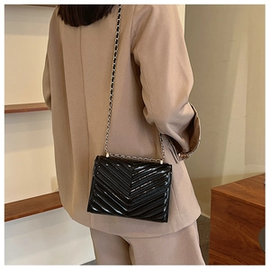 Detail of black patent leather crossbody bag with V-shaped quilting and gold chain strap