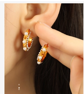 Detailed close-up of gold C-shaped hoop earrings with inlaid pearls and metal studs