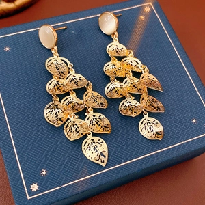 Macro shot of long gold hollow leaf tassel earrings with cat eye stones on jewelry box