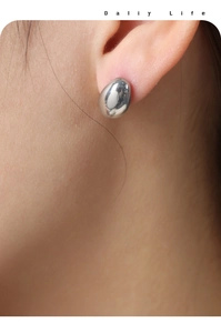 Close-up of polished silver pebble stud earrings showing minimalist aesthetic on model